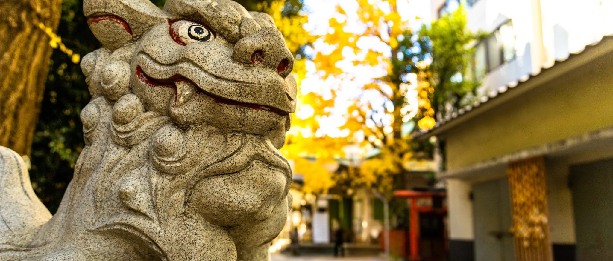 黄色い落ち葉に囲まれた、神社の石造りの狛犬