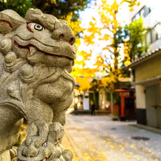 黄色い落ち葉に囲まれた、神社の石造りの狛犬