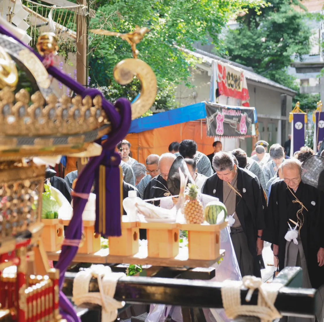 神輿の前で、和装の参加者たちが頭を下げて祈りを捧げる様子
